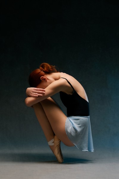portrét baletky v modrej sukienke, objímajúcej si rukami kolená
