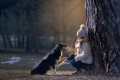 fotka dievčatka opierajúceho sa o strom a psa border collie podávajúceho mu labku